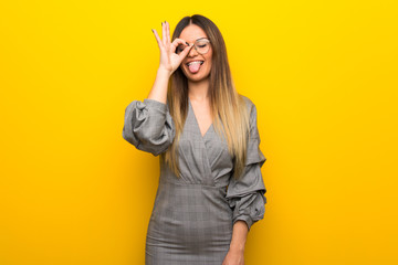 Young woman with glasses over yellow wall makes funny and crazy face emotion