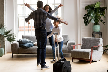 Happy loving black family wife and kid daughter excited to meet hurry to hug dad with suitcase coming returning home arriving from long business trip, welcome back african father, reunion concept