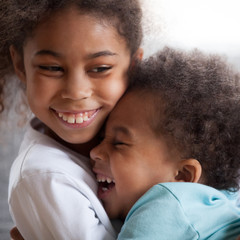 Cute african american kids with funny faces hugging laughing, 2 siblings boy and girl embracing...