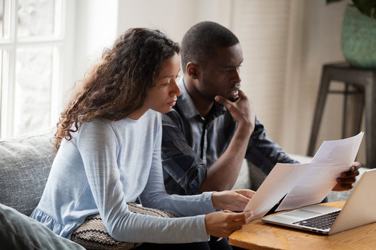 Serious worried african american couple reading documents consider mortgage loan insurance contract terms, focused black man and woman holding checking bank papers at home, domestic bills concept