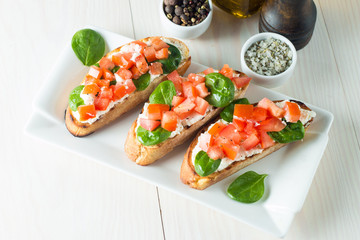 Tomato and cheese fresh made bruschetta. Italian tapas, antipasti with vegetables, herbs and oil on grilled ciabatta and baguette bread. Sandwich.