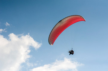 Alone paraglider flying in the blue sky against the background of clouds. Paragliding in the sky on a sunny day.