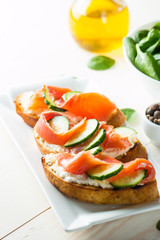 Salmon, cucumber and cream cheese bruschetta. Italian tapas, antipasti with vegetables, herbs and oil on grilled ciabatta and baguette bread. Sandwich.