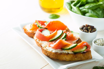 Salmon, cucumber and cream cheese bruschetta. Italian tapas, antipasti with vegetables, herbs and oil on grilled ciabatta and baguette bread. Sandwich.