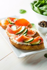 Salmon, cucumber and cream cheese bruschetta. Italian tapas, antipasti with vegetables, herbs and oil on grilled ciabatta and baguette bread. Sandwich.