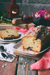 Dried fruit cake with raisins, apricots, cherry and glass of red wine, bottle and flower rustic wooden background. Valentines day still life. Sliced freshly baked fruitcake. Copy space for text
