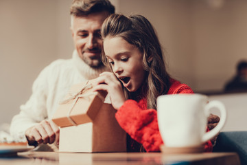 Young girl opening brown present box in cafe