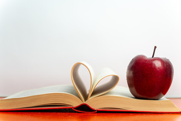 on the table there is an open book with a red cover, next to a red apple