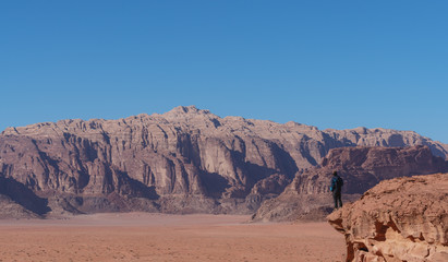 Traveler standing on edge of mountain cliff, at Wadi Rum desert in Jordan. Travel lifestyle and adventure and journey