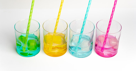 colored glasses in a row with colored ice and drinking straws filled with cold, fresh water