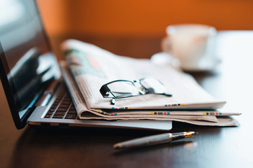 Laptop, newspaper and glasses on the table.