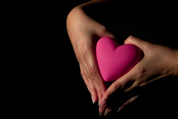 Female hands holding pink heart shape on a black background. Symbol, Human Hand