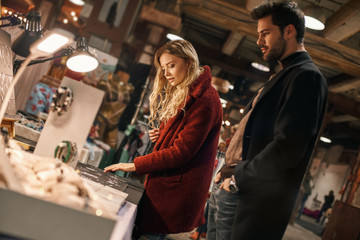 Happy young couple choosing handmade imitation jewelry at small street market