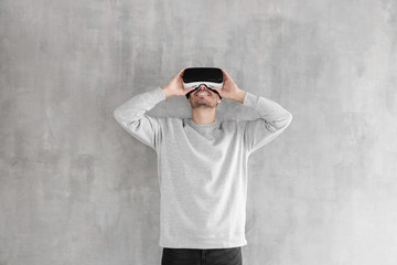Handsome man experiencing virtual reality using VR headset glasses, playing video games, standing against gray wall