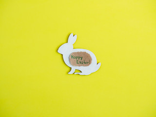 Wooden figure of the rabbit, painted white, on a yellow, isolated background. Top view, closeup. Happy Easter. Preparation for the holiday