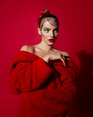 Beautiful attractive girl with smooth hair and in a red fur coat made of faux fur posing in the studio on a red background.