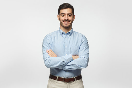 Modern business man in casual blue shirt standing with crossed arms, isolated on gray background
