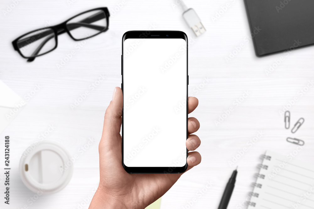 Poster Modern smart phone ih hand with isolated, blank display for mockup, ap design presentation. Office desk in background.