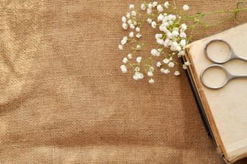 Vintage spring background with white flowers, a yellowed old books and the scissors on the burlap. closeup. topview
