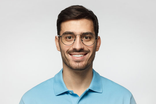 Close up portrait of young smiling handsome guy in blue polo shirt and round glasses, isolated on gray background