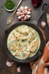Chicken fillet or Turkey breast in creamy sauce with dill and garlic, in cast iron black pan on dark background. Delicious homemade food