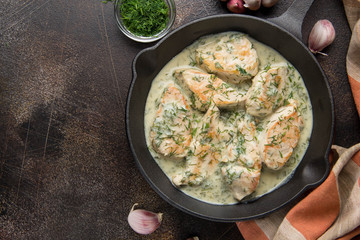 Chicken fillet or Turkey breast in creamy sauce with dill and garlic, in cast iron black pan on dark background. Delicious homemade food