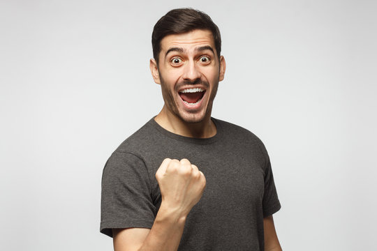 Young excited man celebrating win of his team, raised fist in victory gesture, isolated on gray background