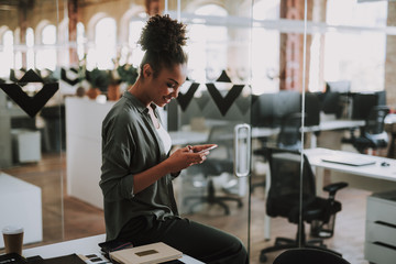 Beautiful afro american girl using cellphone at modern office