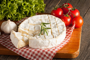 Camembert and brie cheese on wooden background with tomatoes, letuce and garlic. Italian food. Dairy products.