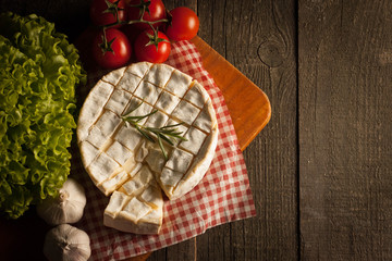 Camembert and brie cheese on wooden background with tomatoes, letuce and garlic. Italian food. Dairy products.