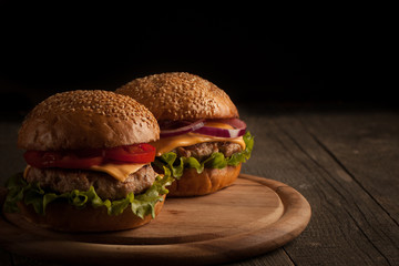 Home made hamburger with beef, onion, tomato, lettuce and cheese. Fresh burger close up on wooden rustic table with potato fries, beer and chips. Cheeseburger.
