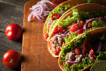 Photo of Mexican tacos with ground beef, onion, tomatoes, chili, red sauce, lettuce and lime on wooden background. Spicy and fast food concept.