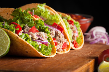 Photo of Mexican tacos with ground beef, onion, tomatoes, chili, red sauce, lettuce and lime on wooden background. Spicy and fast food concept.