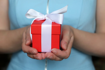 Woman with Valentine gift close up. Female hands holding red gift box with white ribbon, present for birthday or Valentine's day