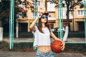 Pretty young sporty girl with basketball ball outdoor.