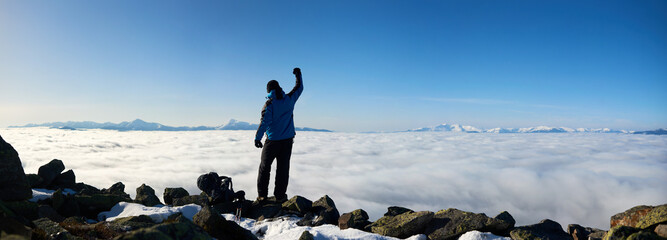 Back view of tourist hiker man with raised arm standing on rocky hill on copy space background of...