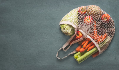 Various farm organic vegetables from local market in net string shopping bag on rustic background, top view with copy space for your design, banner. Clean and healthy food concept. Seasonal vegetable