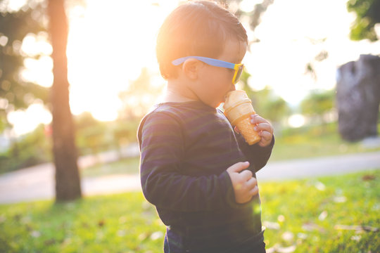 Happy little Asian boy eating ice cream cone with sun glasses in the garden, soft focus