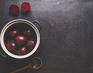 Whole boiled beet roots in cooking pot with wooden spoon on dark background, top view with copy...