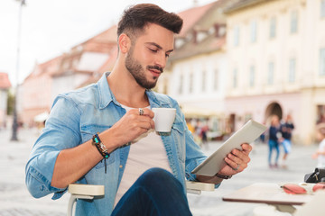 relaxed man drinking coffee looks at tablet in the city