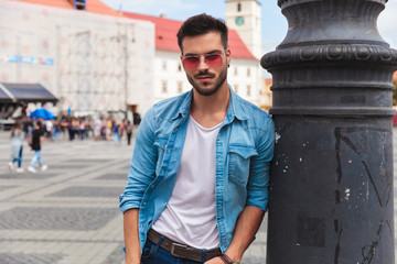 relaxed man in denim shirt leans against lighting pole