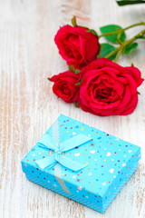 Fresh red roses and gift box on wooden table