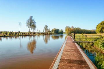 Obraz premium A long jetty along the river Linge in the Betuwe region with a row of cut willows on the other side