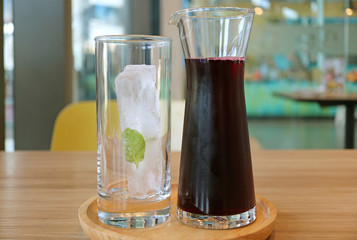 A Carafe of Roselle Juice with a Glass of Ice Cube on Wooden Tray Served on Wooden Table 