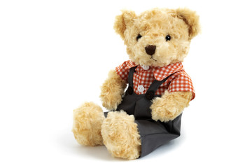 Dressed toy teddy bear in shirt and trousers is sitting on white background