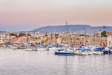 Fototapeta na wymiar Travel Concepts. Picturesque Image of Old Venetian Harbour of Chania with line of Fisihing Boats and Yachts in the Foregound Against Clear Sky in Crete
