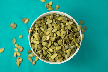 Bowl full of pumpkin seeds on turquoise background