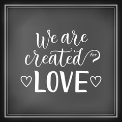 Modern calligraphy lettering of We are created for love in white on chalkboard background decorated with hearts and frame for decoration, poster, banner, valentine, valentines day, sticker, postcard