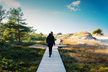 Back view of a young girl walking on a wooden boardwalk path in the beach dunes Nationalpark...