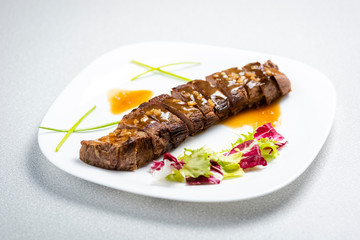 a sliced steak poured with onion decorated with lettuce leaves
